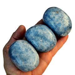 Three big blue calcite tumbled stones on hand with white background