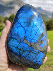 One large blue flash labradorite free form on hand with mountain landscape background