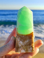 Green caribbean calcite crystal obelisk on hand with beach lansdcape
