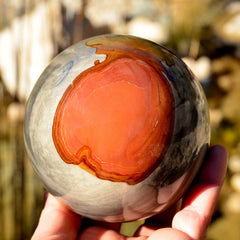Large polychrome jasper crystal sphere 100mm on hand with river plants