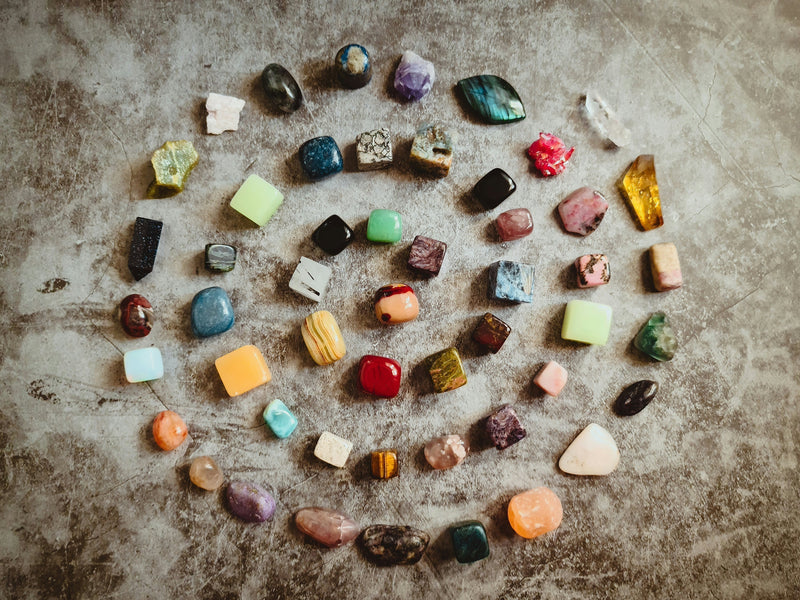 Several different tumbled crystals forming a spiral on a stone table