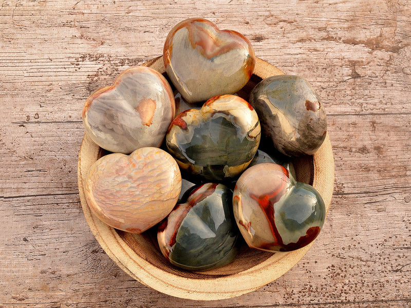 Several large polychrome jasper heart crystals 70mm inside a wood bowl on wood  table