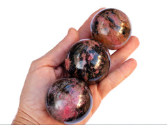 Three pink rhodonite sphere stones 45mm-50mm on hand with white background