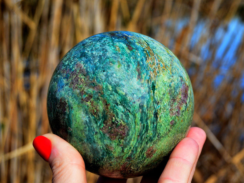 Large chrysocolla sphere crystal 90mm on hand with baackground with river cane plants