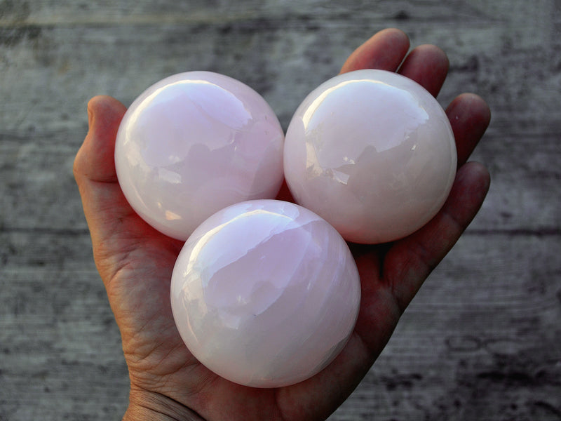 Three pink mangano calcite sphere crystals 50mm-55mm on hand with wood background