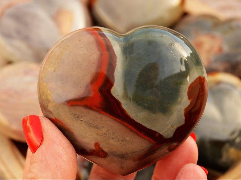 One large polychrome jasper carving heart crystal 70mm on hand with background with some hearts