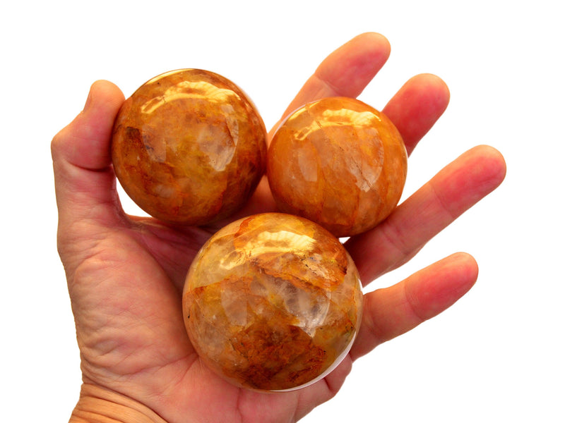 Three golden healer quartz spheres 45mm-60mm on hand with white background