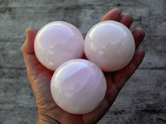 Three pink mangano calcite sphere crystals 50mm-55mm on hand with wood background