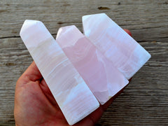 Three pink mangano calcite crystal obelisks 80mm-100mm on hand with wood background