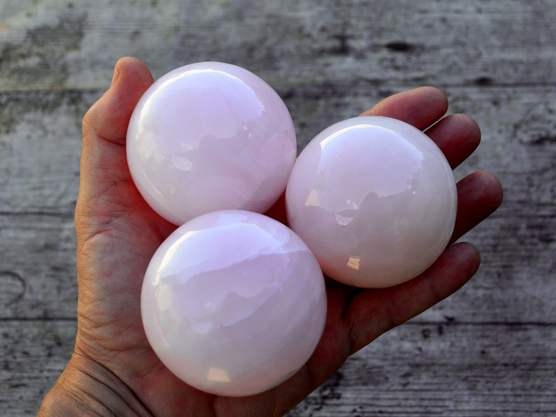 Three pink mangano calcite crystal balls 50mm-55mm on hand with wood background