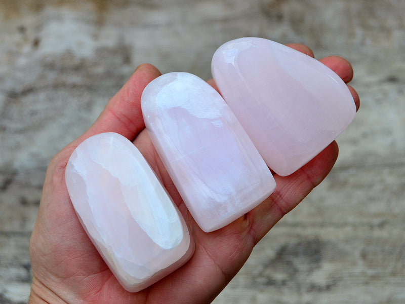 Three pink mangano free form stones 50mm-60mm on hand with wood background