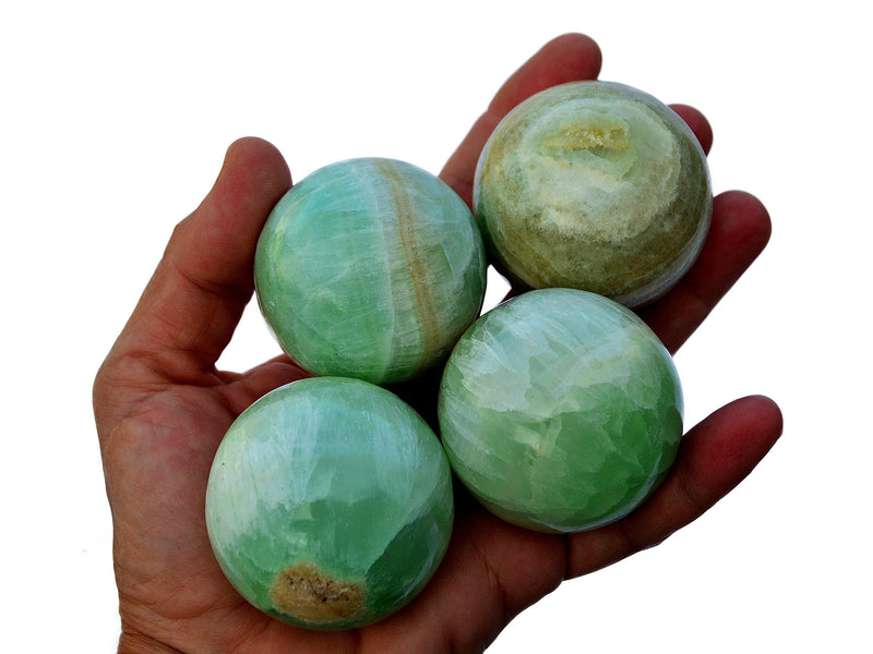 Four pistachio calcite spheres 40mm - 50mm on hand with white background