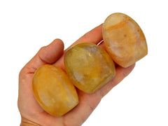 Three small golden healer quartz free forms on hand with white background