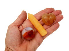 Small faceted orange calcite point, golden healer quartz heart and carnelian sphere on hand with white background