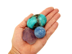 Small raw amethyst, blue calcite sphere and amazonite palm stone on hand with white background