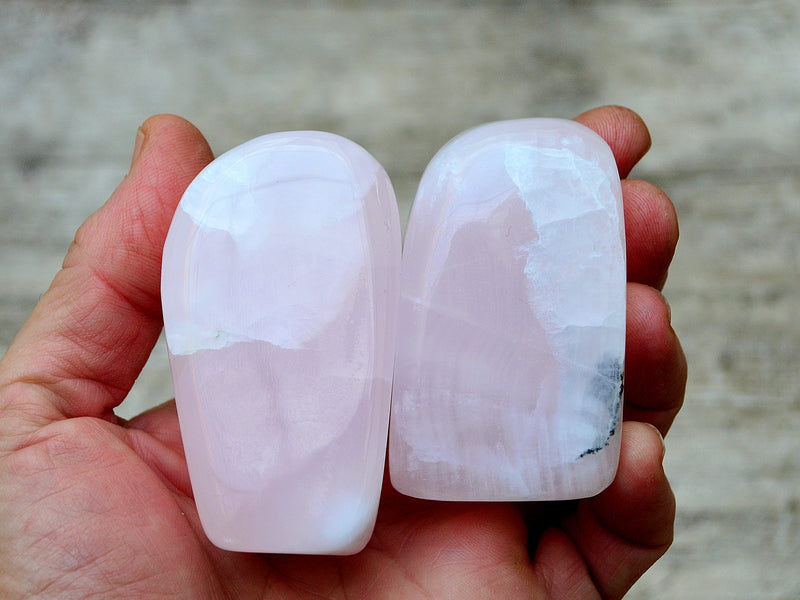 Two pink angano calcite free forms 80mm on hand with wood background