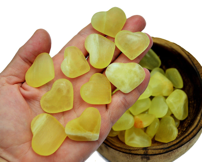 Five lemon calcite crystal hearts 25mm-30mm on hand with background with some stones inside a wood bowl