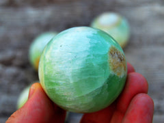 One green pistachio calcite sphere crystal 40mm on hand with background with some balls on wood table