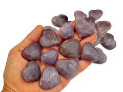 Ten lepidolite crystal hearts 25mm-35mm on hand with background with some crystals on white