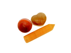 Small orange calcite faceted point, golden healer quartz heart and carnelian sphere on white background