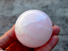 Natural pink mangano calcite sphere 50mm on hand with wood background