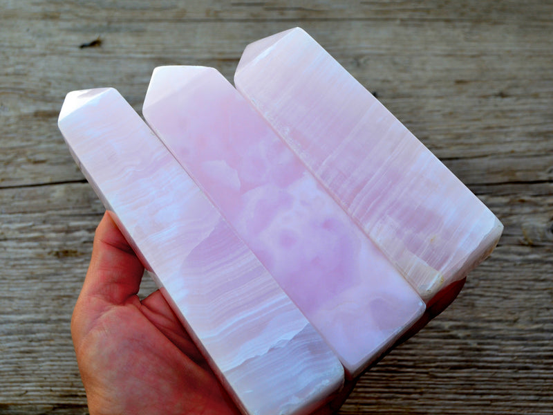 Three pink mangano calcite crystal obelisks 90mm-120mm on hand with wood background