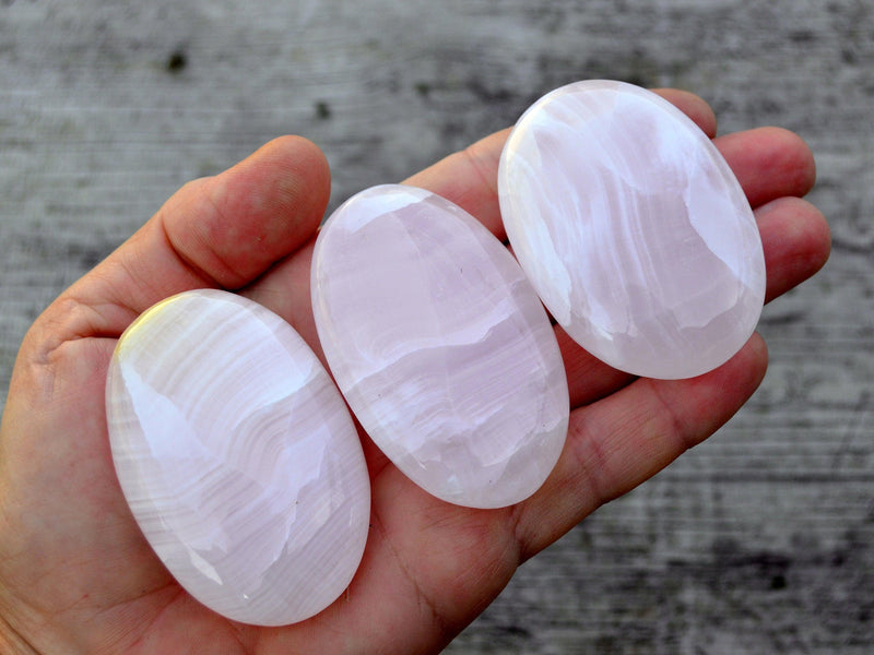 Three pink mangano calcite palm stones 55mm-60mm on hand with wood background