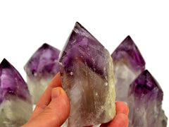 One amethyst semi polished point 65mm on hand with background with some stones on white