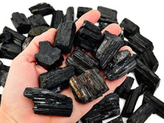 Nine  raw black tourmaline stones 35mm-45mm on hand with background with several crystals on white