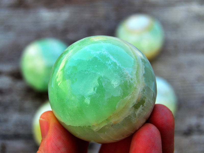 One green pistachio calcite sphere crystal 50mm on hand with background with some balls on wood table