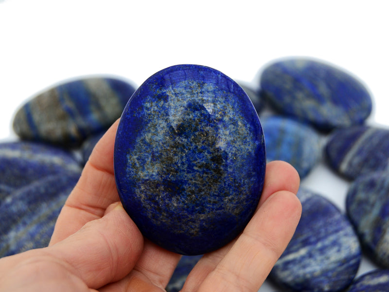 One natural blue lapis lazuli palm stone 65mm on hand with background with some stones on white