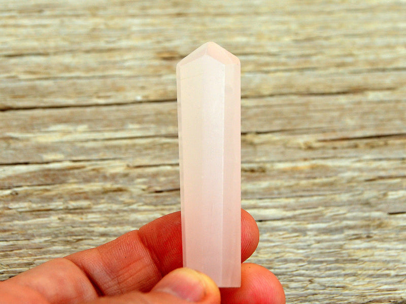 One pink mangano calcite crystal point 55mm on hand with wood background