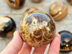 One orbicular brown calcite sphere 55mm on hand with background with some stones on wood table