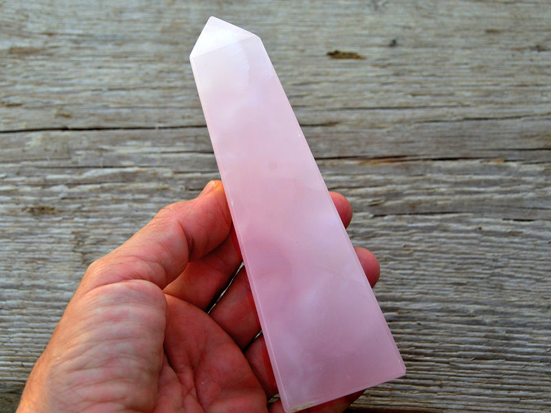 One large pink mangano calcite faceted point 150mm on hand with wood background