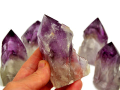 One amethyst semi polished point 80mm on hand with background with some stones on white