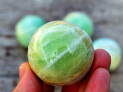 One green pistachio calcite crystal ball 55mm on hand with background with some balls on wood table