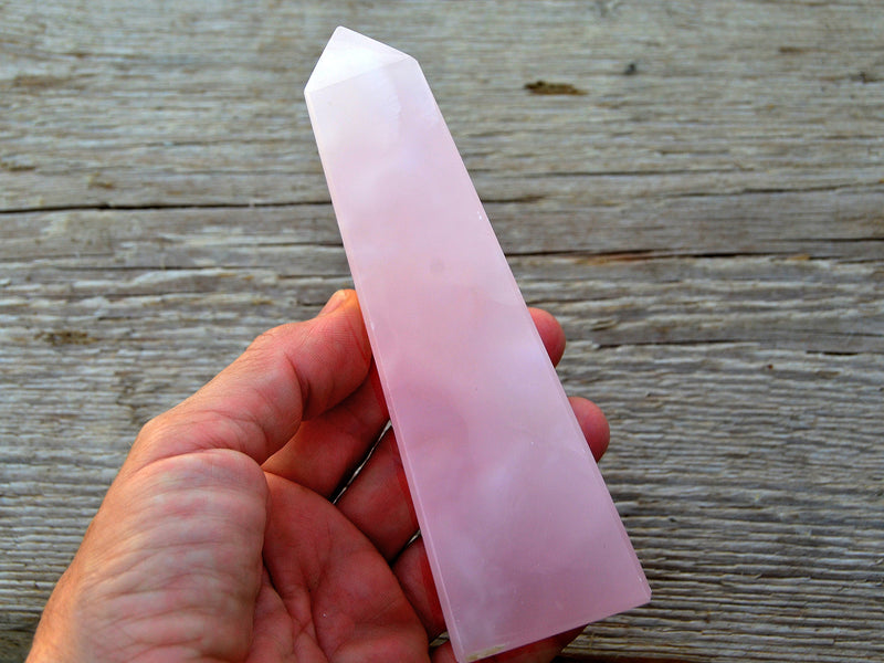 One large pink mangano calcite faceted point 150mm on hand with wood background