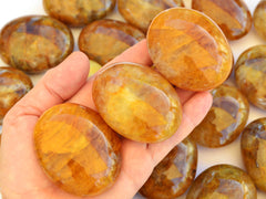 Three yellow hematoid quartz palm stones on hand with background with some crystals on white