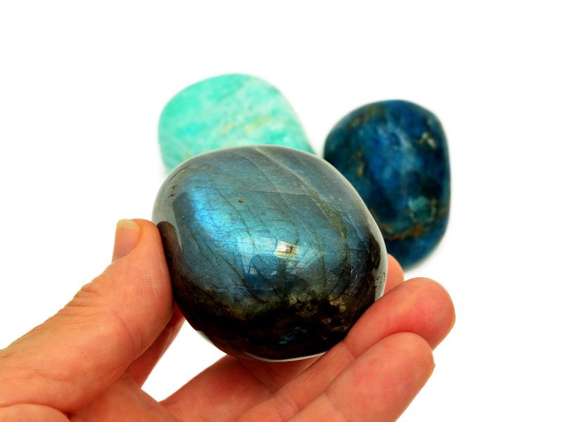 One large labradorite tumbled stone on hand with background with blue apatite and green amazonite