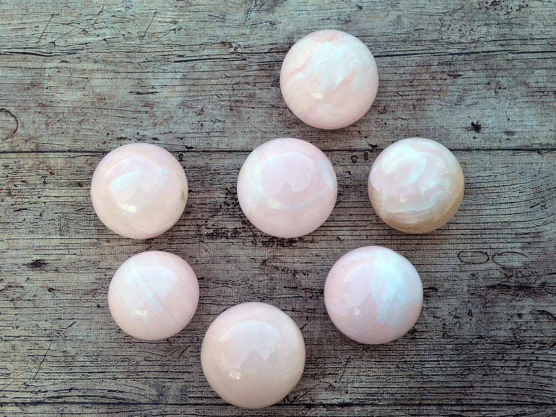 Seven pink mangano calcite crystal spheres 50mm-55mm on wood table