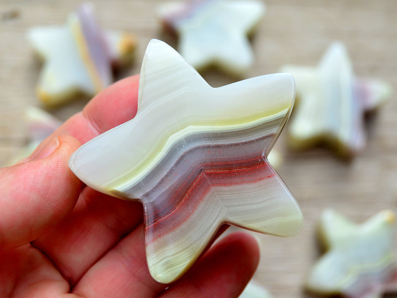 One pink banded onyx star carved crystal 60mm on hand with background with some gemstones on wood t