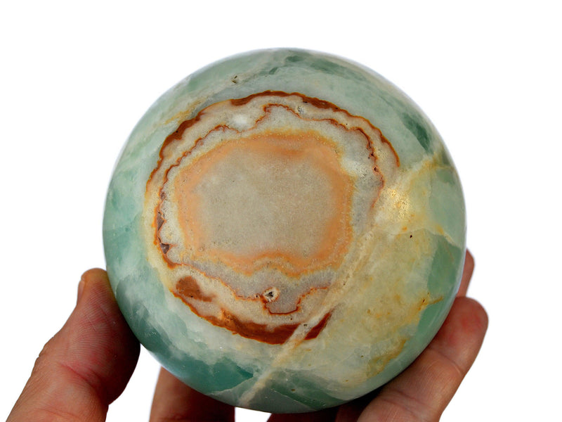 One large caribbean calcite sphere crystal 85mm on hand with white background
