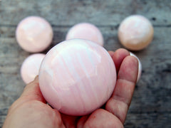 Natural pink mangano calcite sphere 50mm on hand with background with some stones on wood background