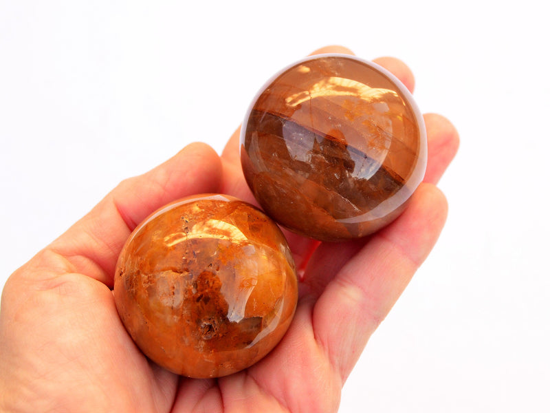 Two yellow hematoid quartz crystal spheres 55mm-60mm on hand with white background
