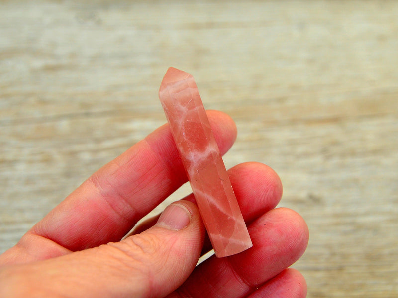 One small rose calcite faceted crystal point 50mm on hand with wood background