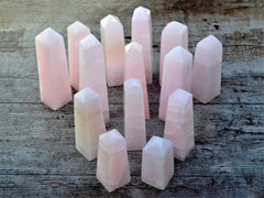 Several large pink mangano crystals obelisks on wood table