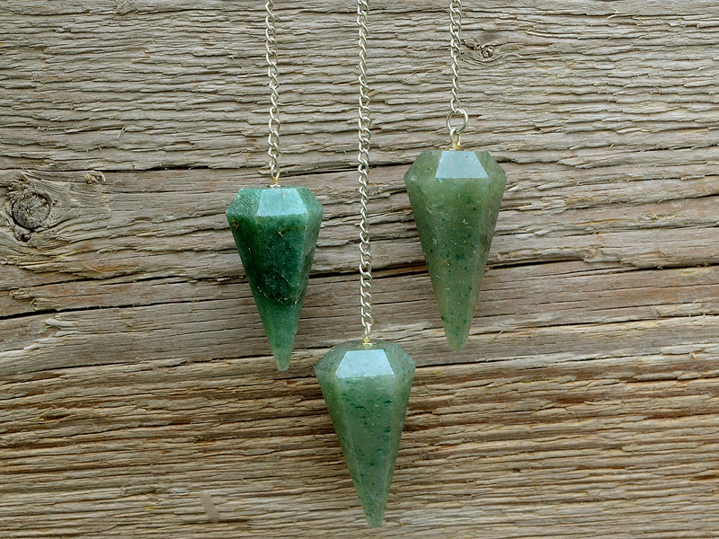 Three green aventurine faceted point pendulums with silver chain hanging on wood background