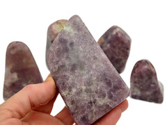 One purple lepidolite free form stone 95mm on hand with background with some crystals on white