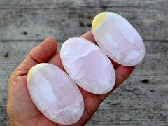 Three pink mangano calcite palm stones 65mm-70mm on hand with wood background