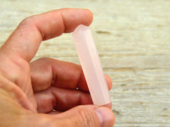 One pink mangano calcite tower crystal 55mm on hand with wood background